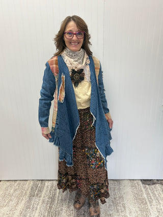 Woman wearing a blue cardigan, floral skirt, and patterned scarf against a white wall.