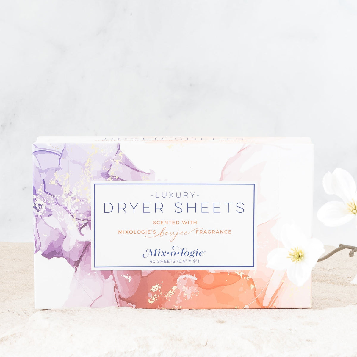 Luxury Dryer Sheets scented with Mixologie's Boujee fragrance. There are 40 sheets in a box, the sheet dimensions are 6.4 inches X 9 inches. Box is purple, pink, and white placed in the sand with white flowers.